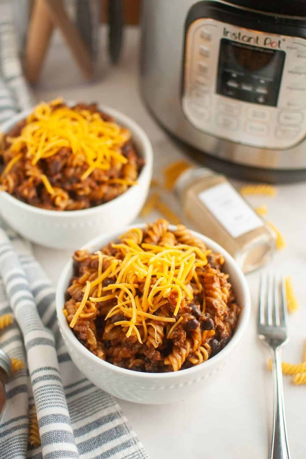two bowls of Instant Pot enchilada pasta casserole, garnished with cheese. A pressure cooker is in the background.