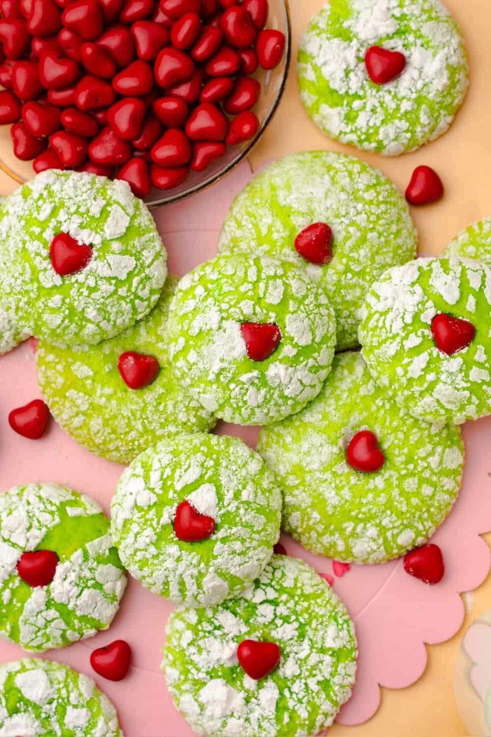 overhead view of several Grinch crinkle cookies next to a bowl of red candy hearts.