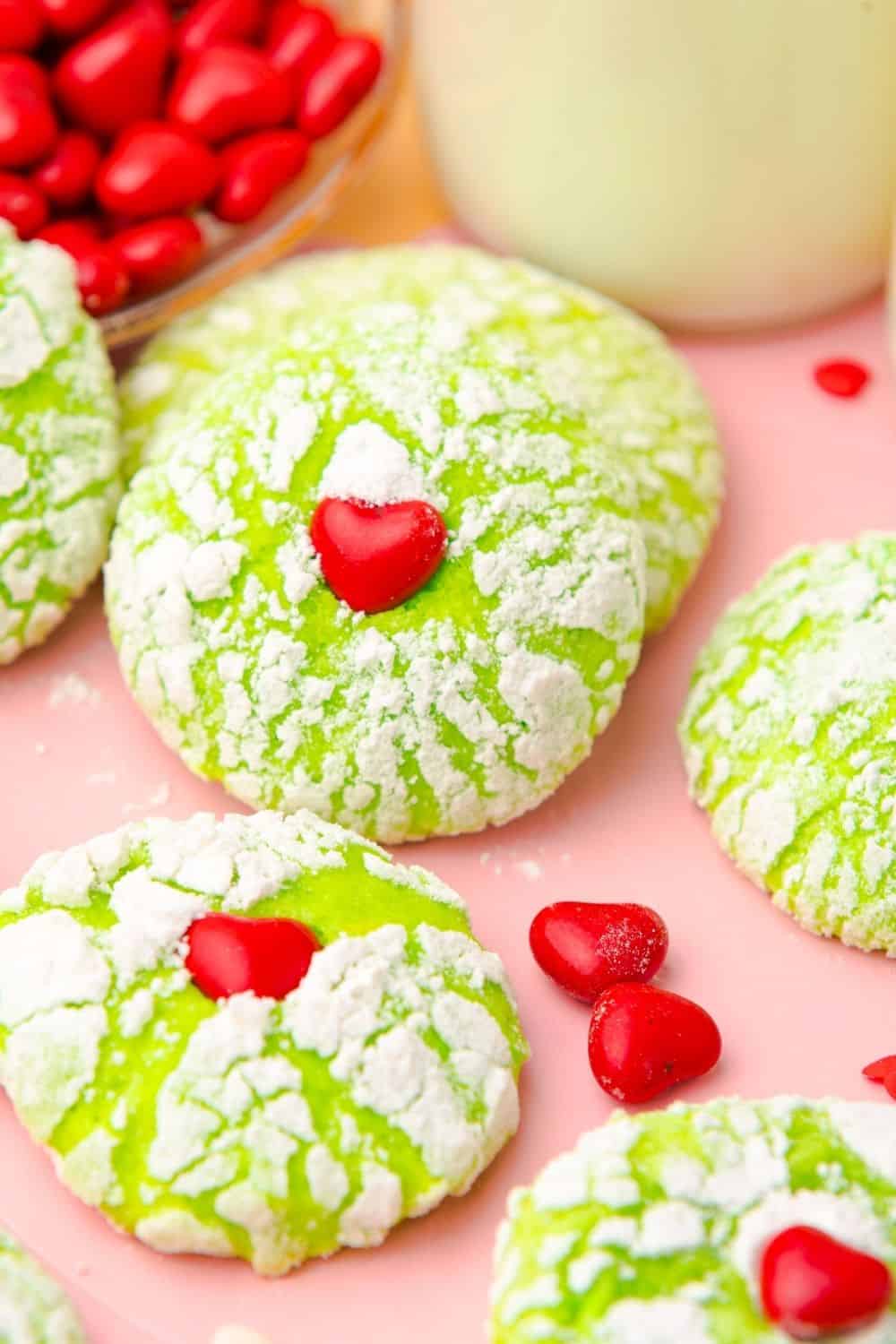 Grinch-themed Christmas cookies on a piece of parchment paper, with red heart candies sprinkled around.