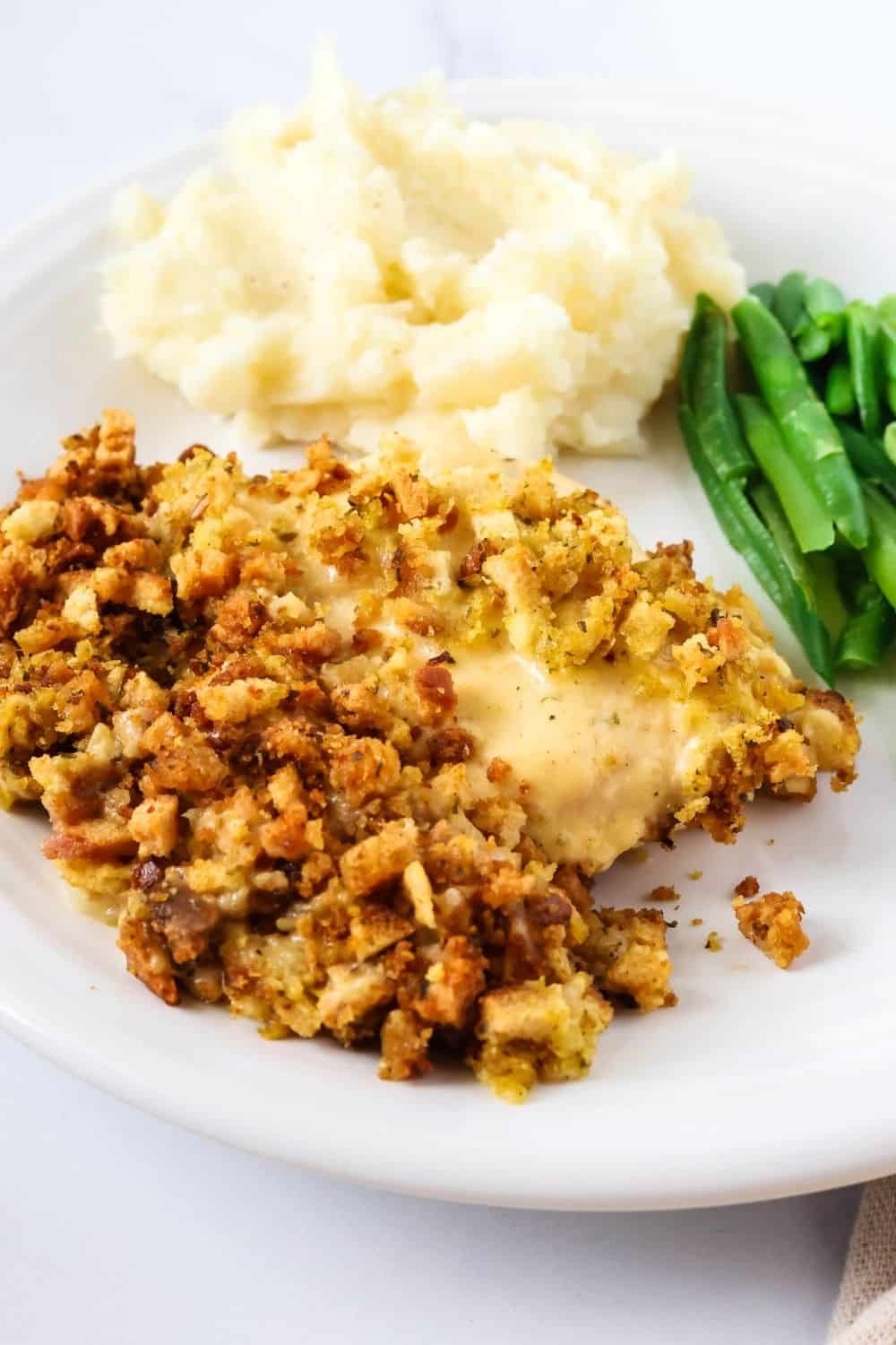 close-up view of a chicken breast, covered in sauce and stuffing. Potatoes and green beans are on the plate as well.