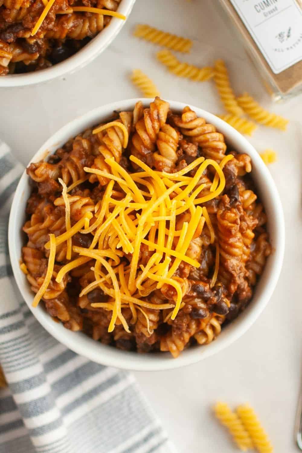 overhead view of a white bowl of Instant Pot enchilada pasta garnished with shredded cheese.