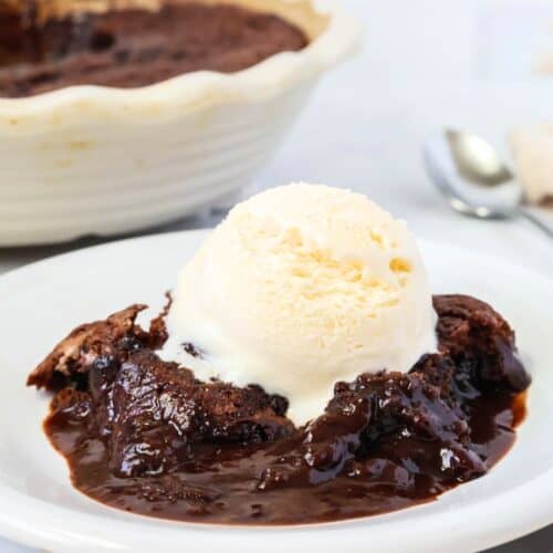 Chocolate cobbler made with Bisquick is served on a white plate, topped with vanilla ice cream. The dish of Bisquick chocolate cobbler is in the background.