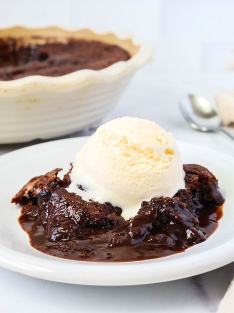 Chocolate cobbler made with Bisquick is served on a white plate, topped with vanilla ice cream. The dish of Bisquick chocolate cobbler is in the background.