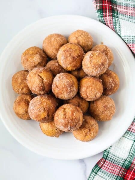 overhead view of Bisquick gingerbread donut holes served on a white plate, with a Christmas plaid kitchen towel next to the plate.