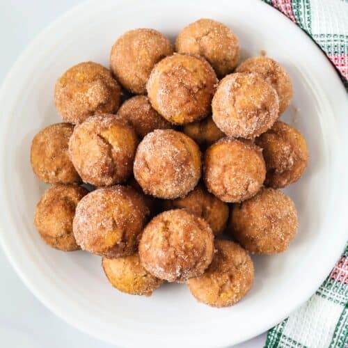 overhead view of Bisquick gingerbread donut holes served on a white plate, with a Christmas plaid kitchen towel next to the plate.