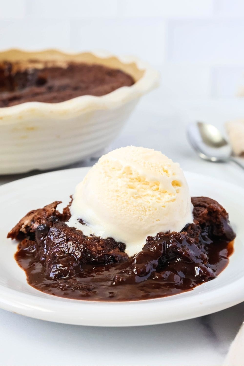 Bisquick molten chocolate cake topped with a scoop of vanilla ice cream. The baking dish of remaining chocolate cobbler is in the background.