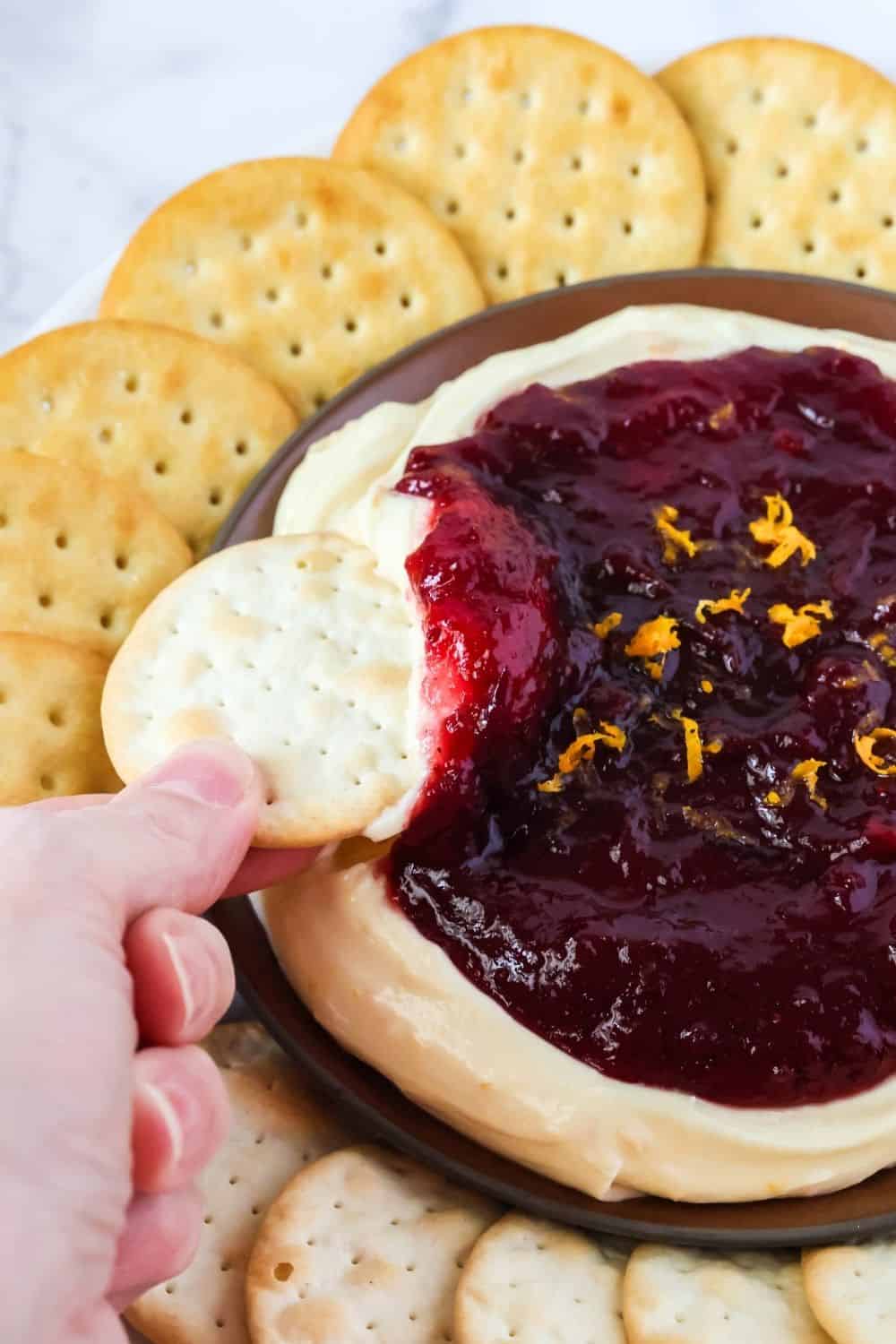 A woman's hand dips a cracker into Christmas cream cheese dip with cranberries.