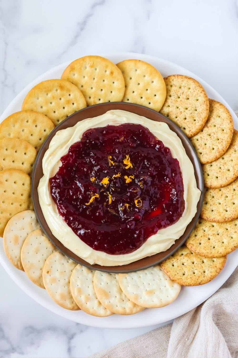 overhead view of a dish of cranberry orange cream cheese spread with different types of crackers spread out around it.