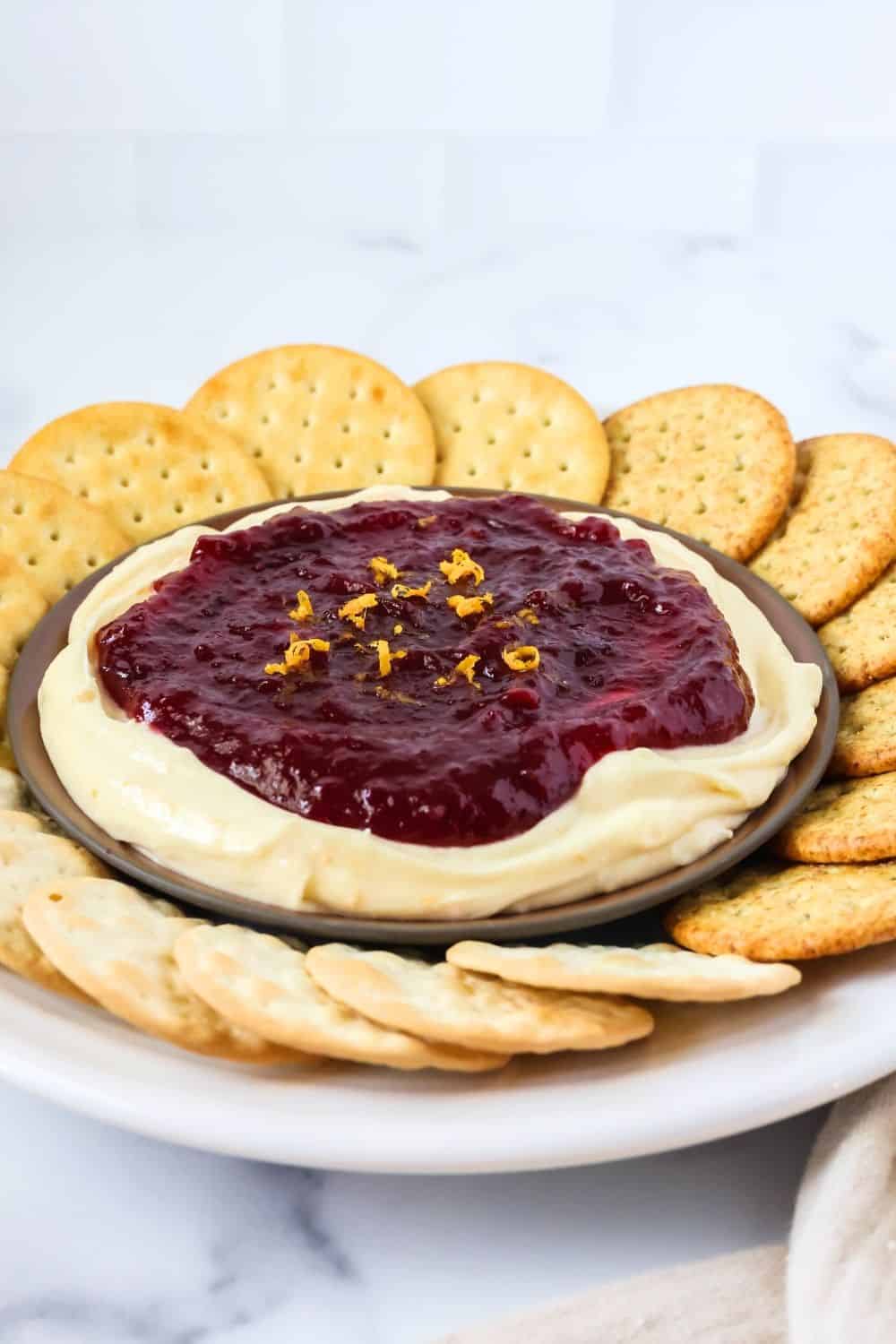 a white plate serves cranberry orange holiday dip surrounded by different types of crackers.