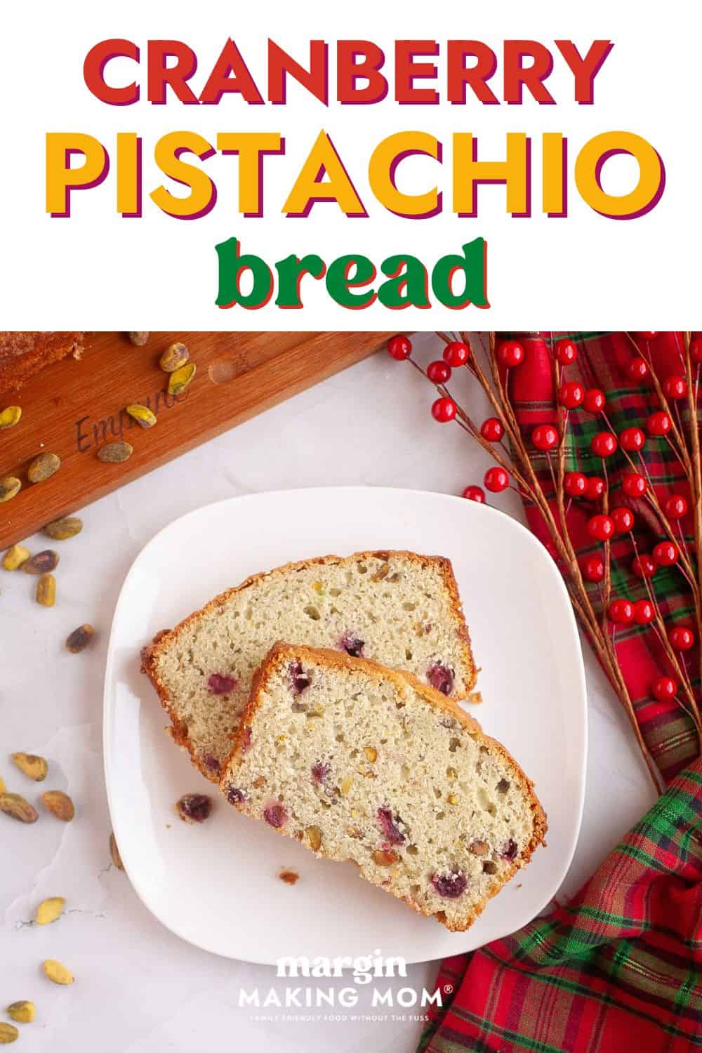 two slices of cranberry pistachio bread served on a white plate, with Christmas decor in the background.