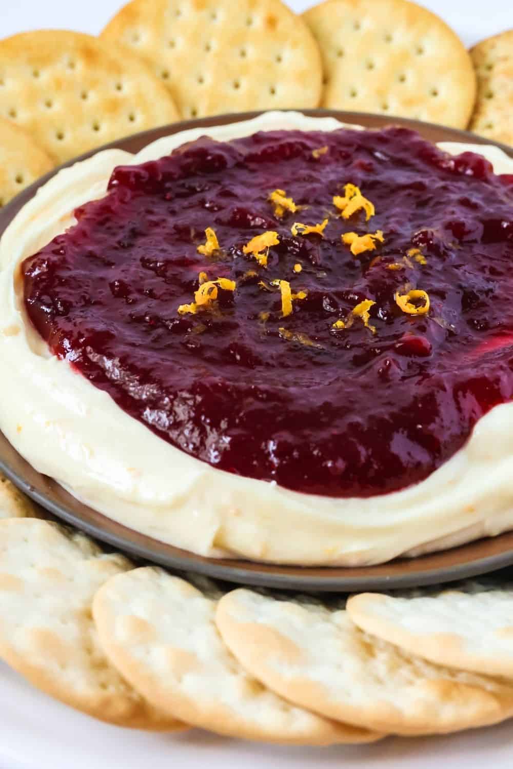 close-up view of cream cheese dip with cranberry sauce on a brown plate, surrounded by crackers.