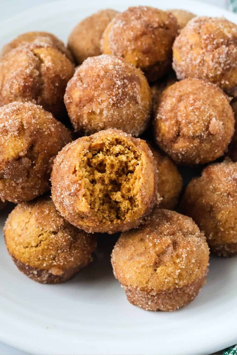 Bisquick gingerbread donut bites on a white plate, one of which has a bite taken out of it, showing the moist interior.