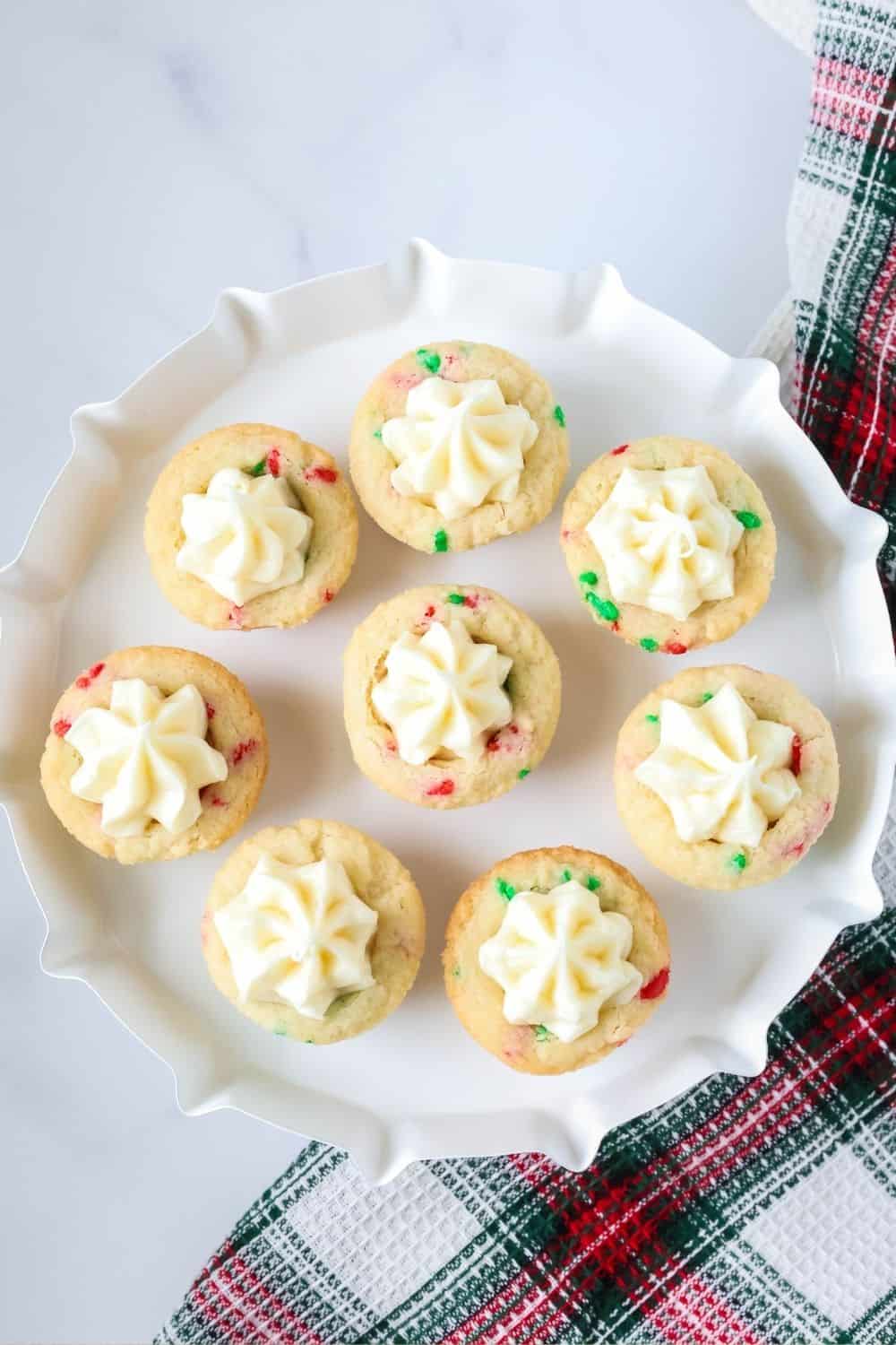 overhead view of several holiday sugar cookie cups filled with vanilla frosting, served on a white dessert stand.