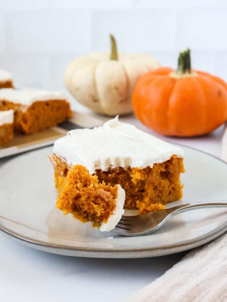 close up of a sheet pan pumpkin bar made with Bisquick. A fork has cut a bite out of the bar. Two small pumpkins are in the background.