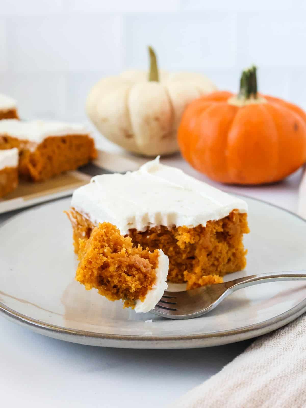 close up of a sheet pan pumpkin bar made with Bisquick. A fork has cut a bite out of the bar. Two small pumpkins are in the background.