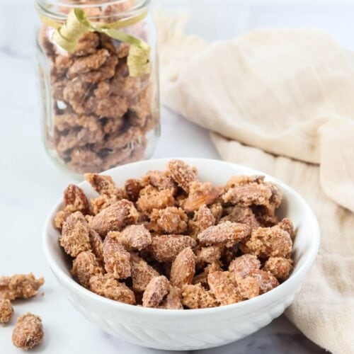 Stovetop cinnamon sugar candied almonds in a white bowl; with more candied almonds in a glass jar in the background.