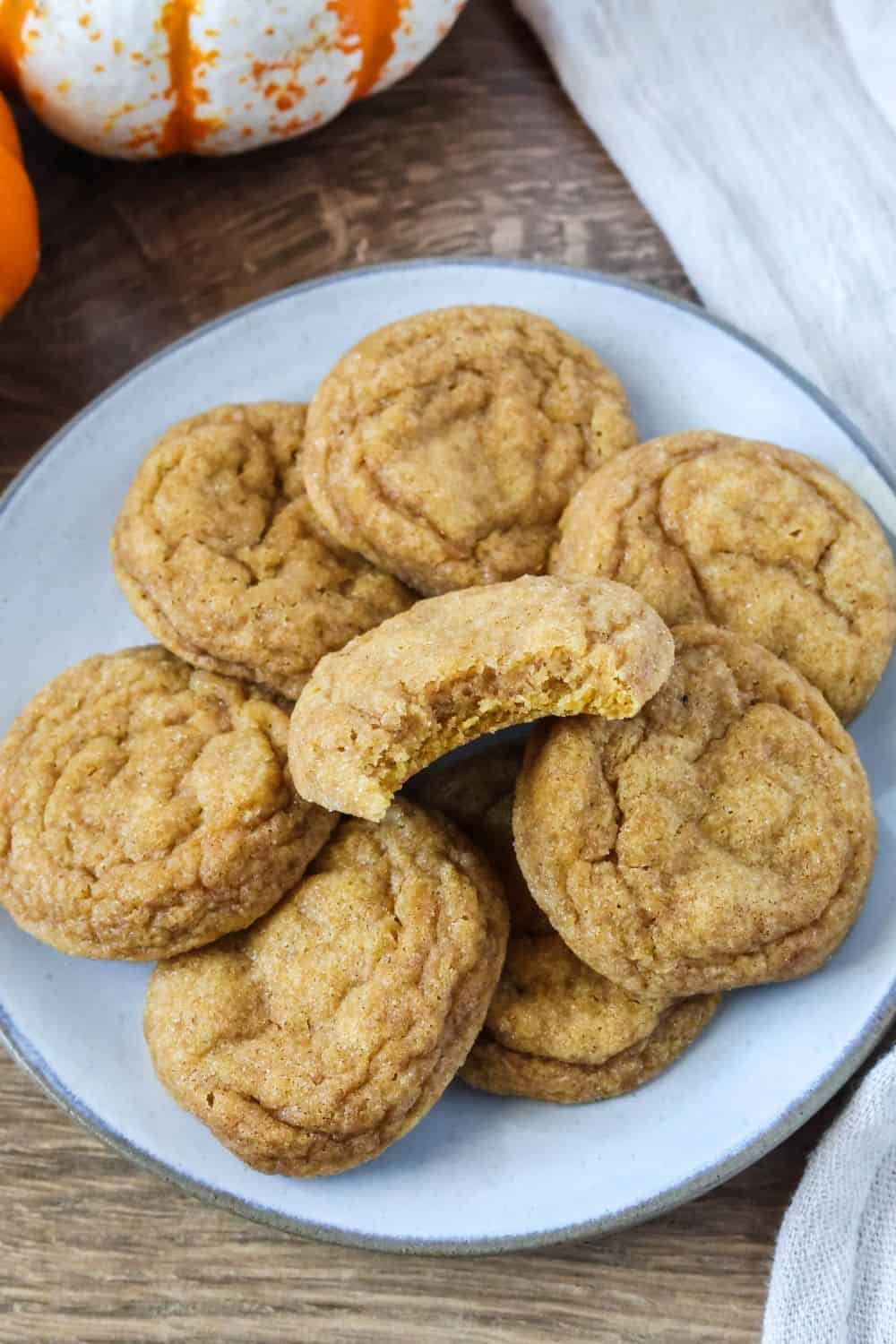 a Plate of soft pumpkin spice snickerdoodles, one of which has a bite taken out of it, showing the chewy interior.