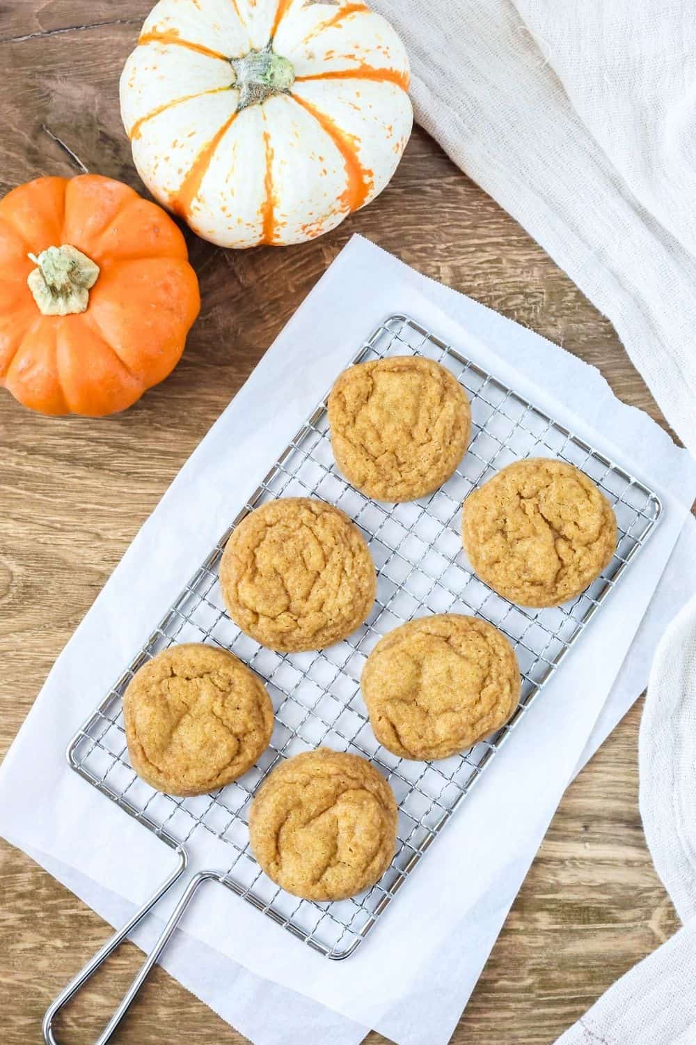 overhead view of six pumpkin snickerdoodle cookies on a wire rack placed on a sheet of parchment.