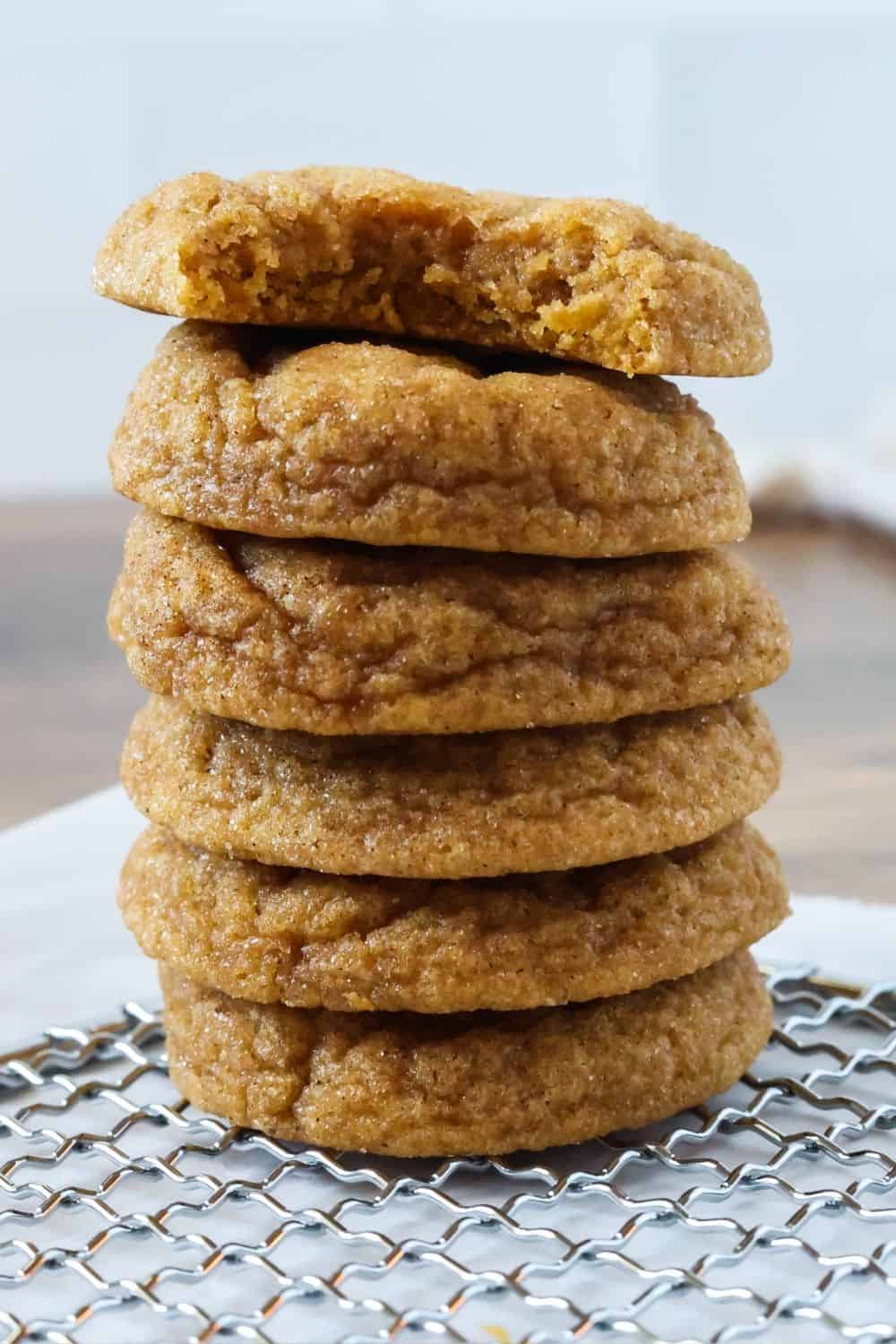 close-up view of a stack of soft and chewy pumpkin snickerdoodle cookies resting on a wire rack. The top cookie has a bite taken out of it.