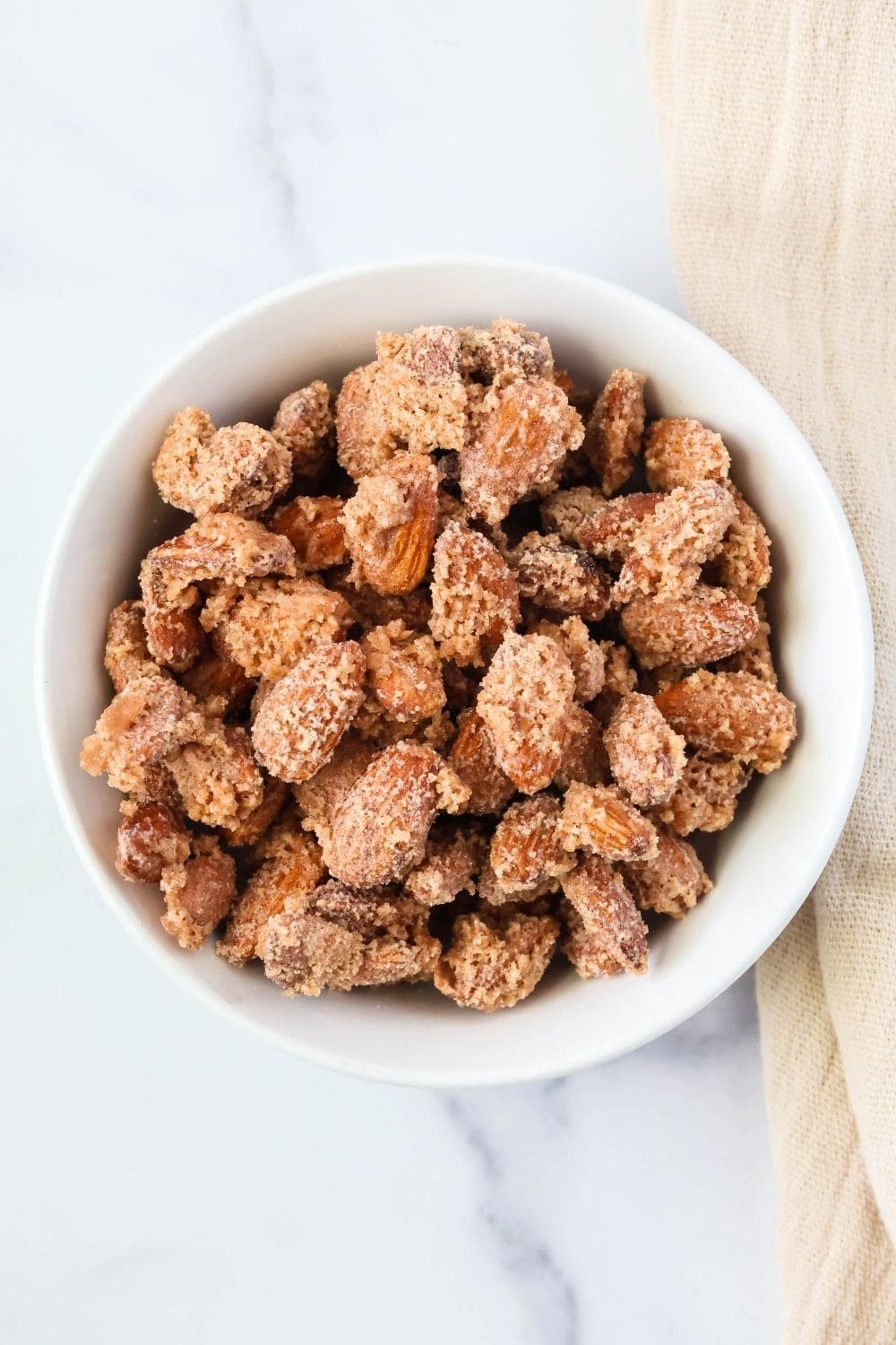 overhead view of a white bowl filled with cinnamon almonds cooked on the stove.