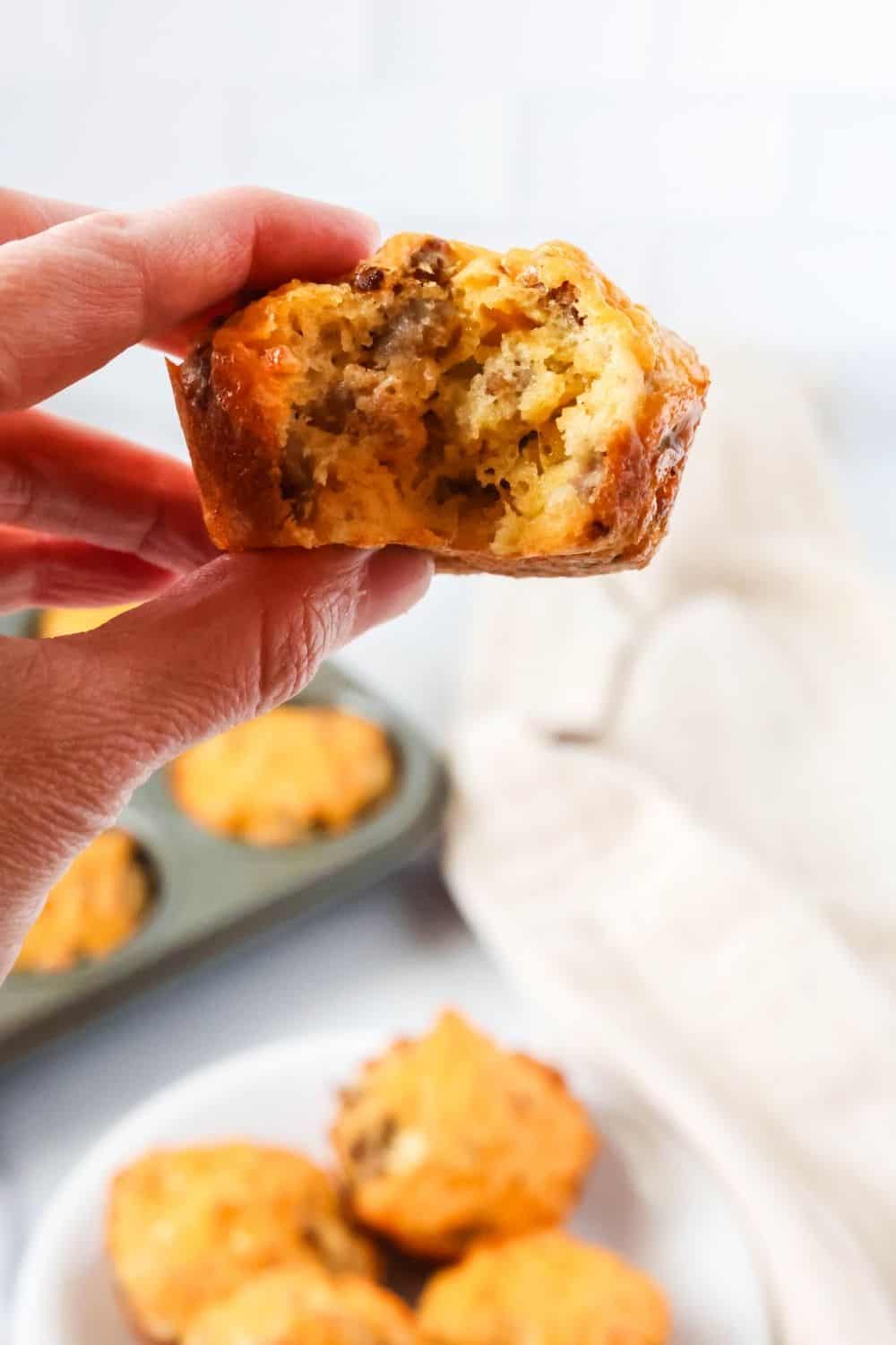 a hand holds a Bisquick sausage muffin with a bite taken out of it.