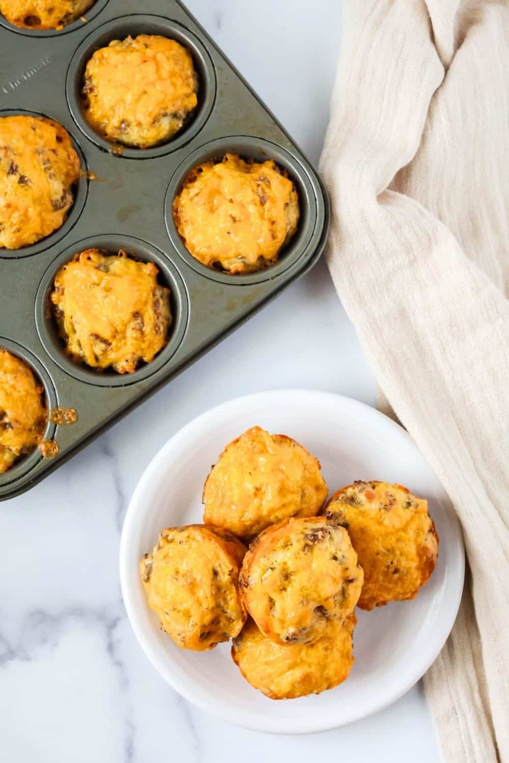 overhead view of Bisquick baking mix sausage muffins on a white plate, with more cheesy egg muffins in the pan.