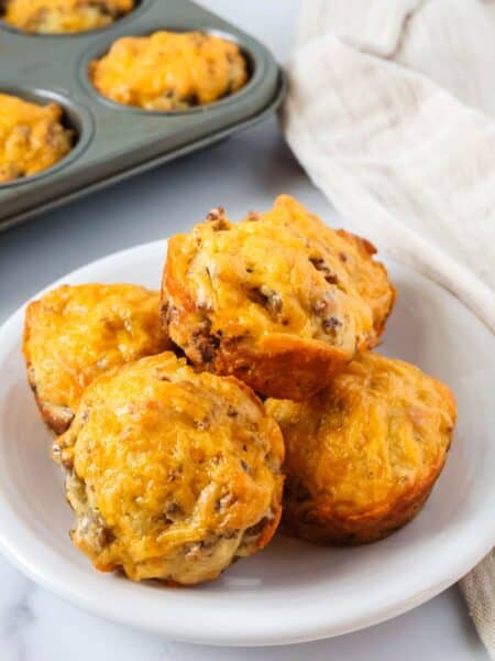 Bisquick sausage muffins on a white plate, with a muffin pan of additional muffins in the background.