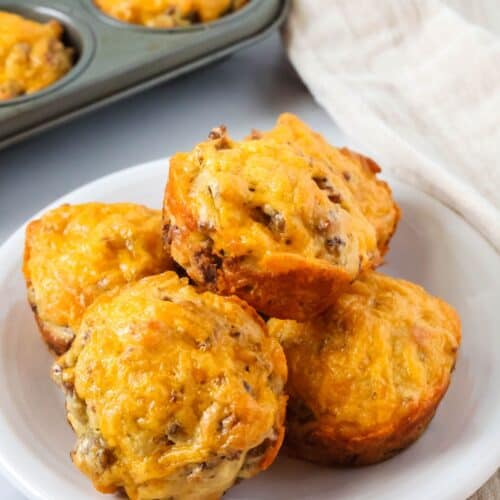 Bisquick sausage muffins on a white plate, with a muffin pan of additional muffins in the background.