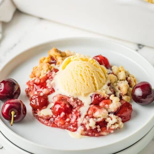 Cake mix cherry cobbler topped with vanilla ice cream and served on a white plate.