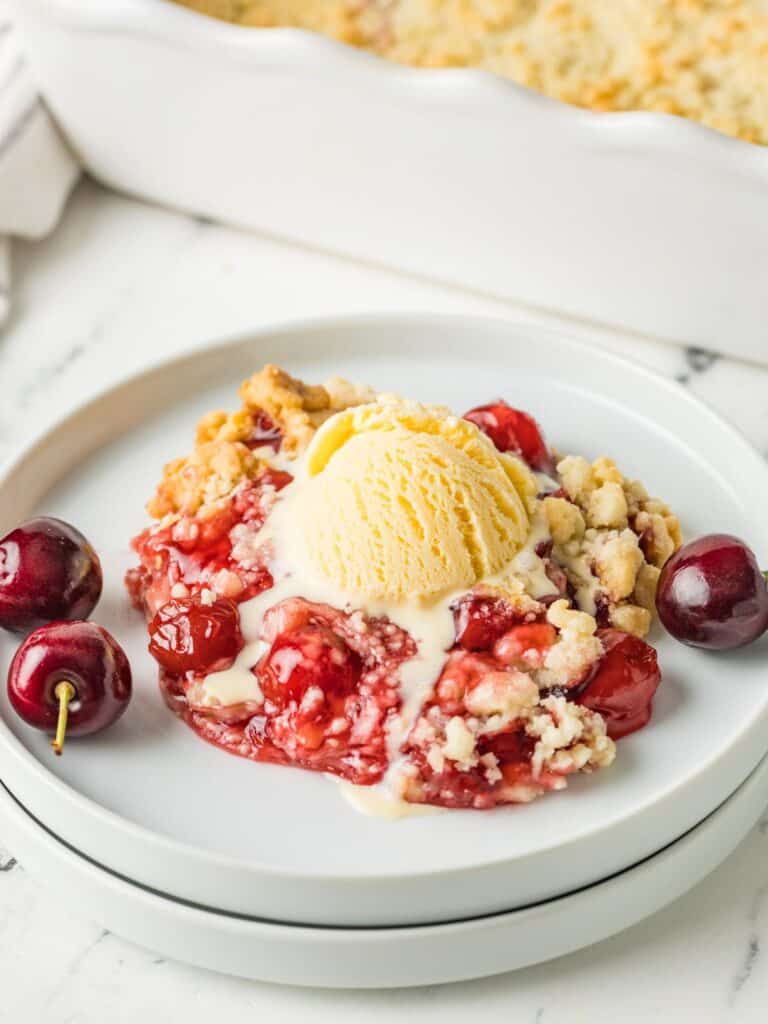 Cake mix cherry cobbler topped with vanilla ice cream and served on a white plate.
