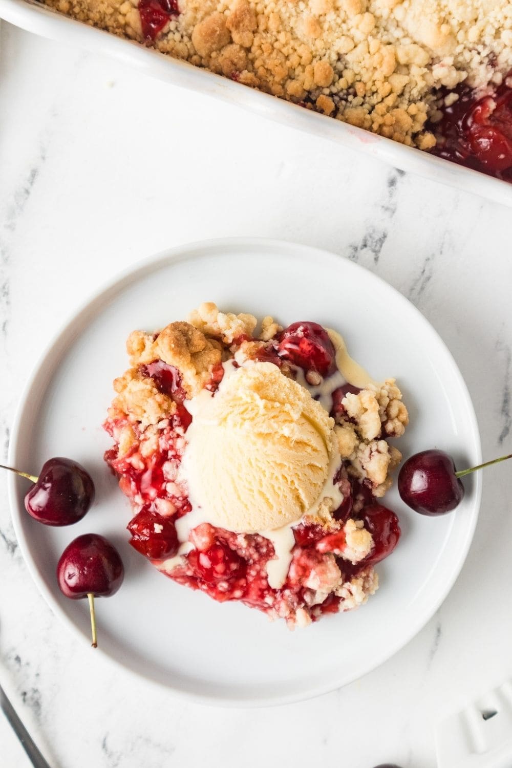 overhead view of a serving of cherry cobbler dump cake served on a white plate, garnished with cherries.