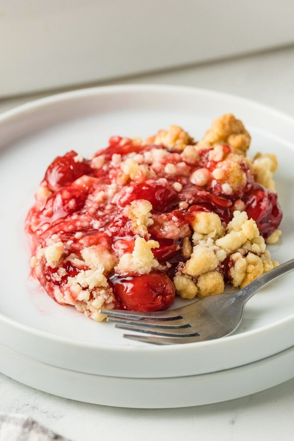 close-up view of cherry cobbler made with yellow cake mix and canned pie filling, served on a white plate alongside a fork.