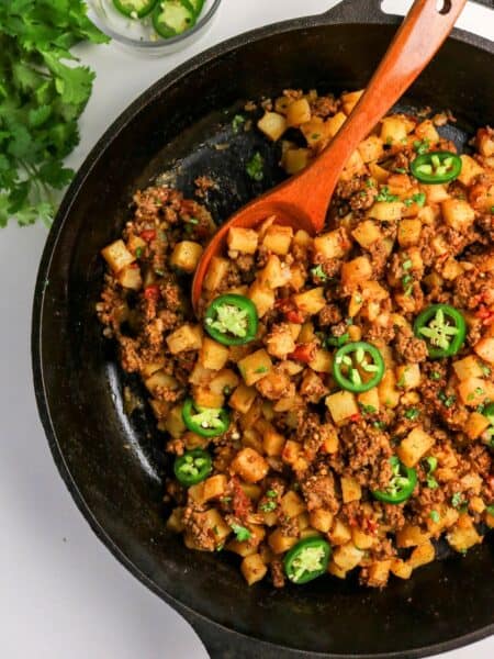 Mexican ground beef and potatoes, AKA picadillo con papas, in a cast iron skillet with a wooden spoon.