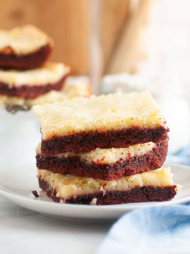 Red velvet ooey gooey butter cake squares stacked together on a white plate.