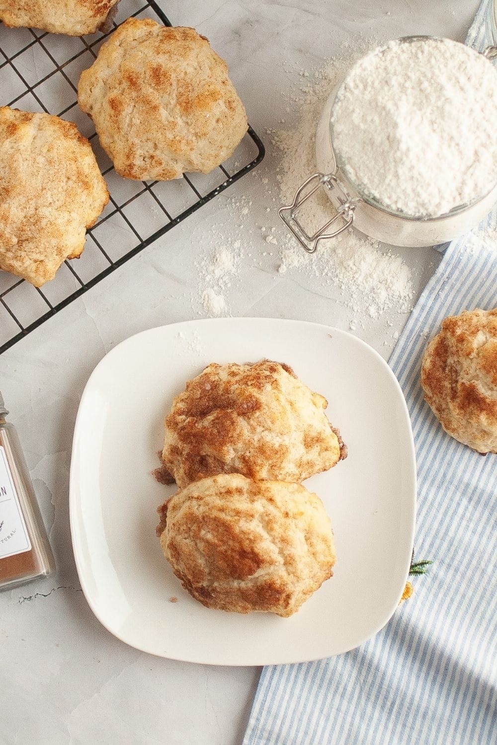overhead view of cinnamon sugar biscuits with glaze, served on a white plate, with additional biscuits and flour in the background.