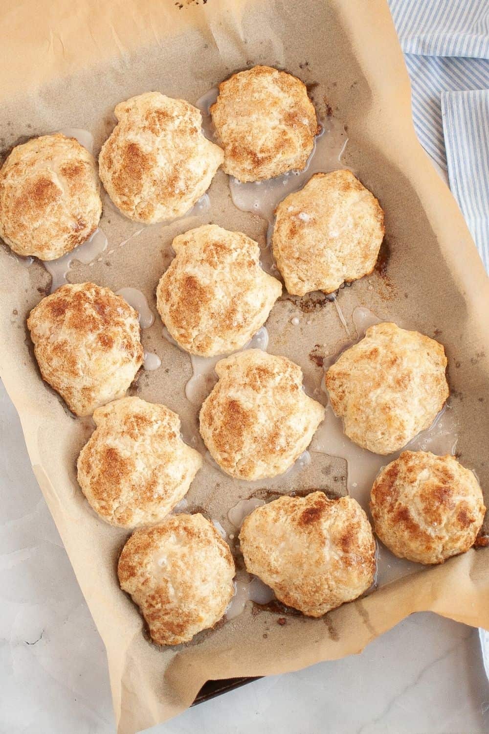 overhead view of cinnamon sugar drop biscuits with glaze, on a parchment-lined baking sheet.