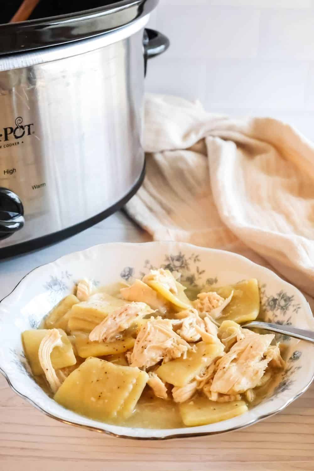a blue and white bowl serves Crock Pot chicken and dumplings. The slow cooker is in the background.