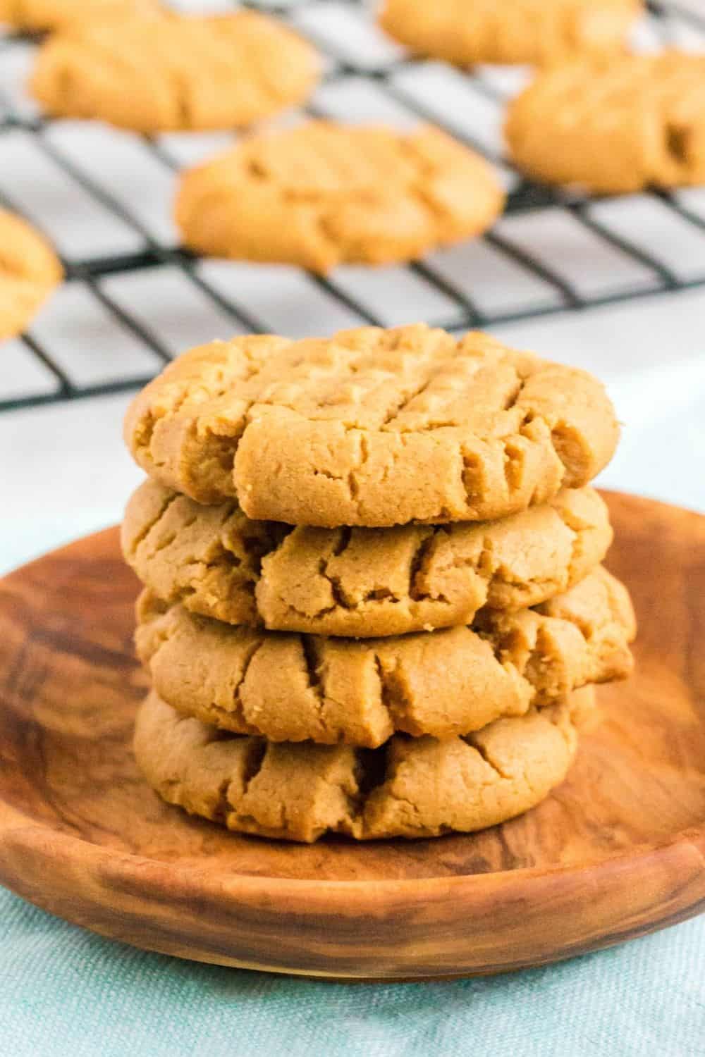 a stack of 5 ingredient peanut butter cookies on a small wooden plate, with more cookies on a wire rack in the background.