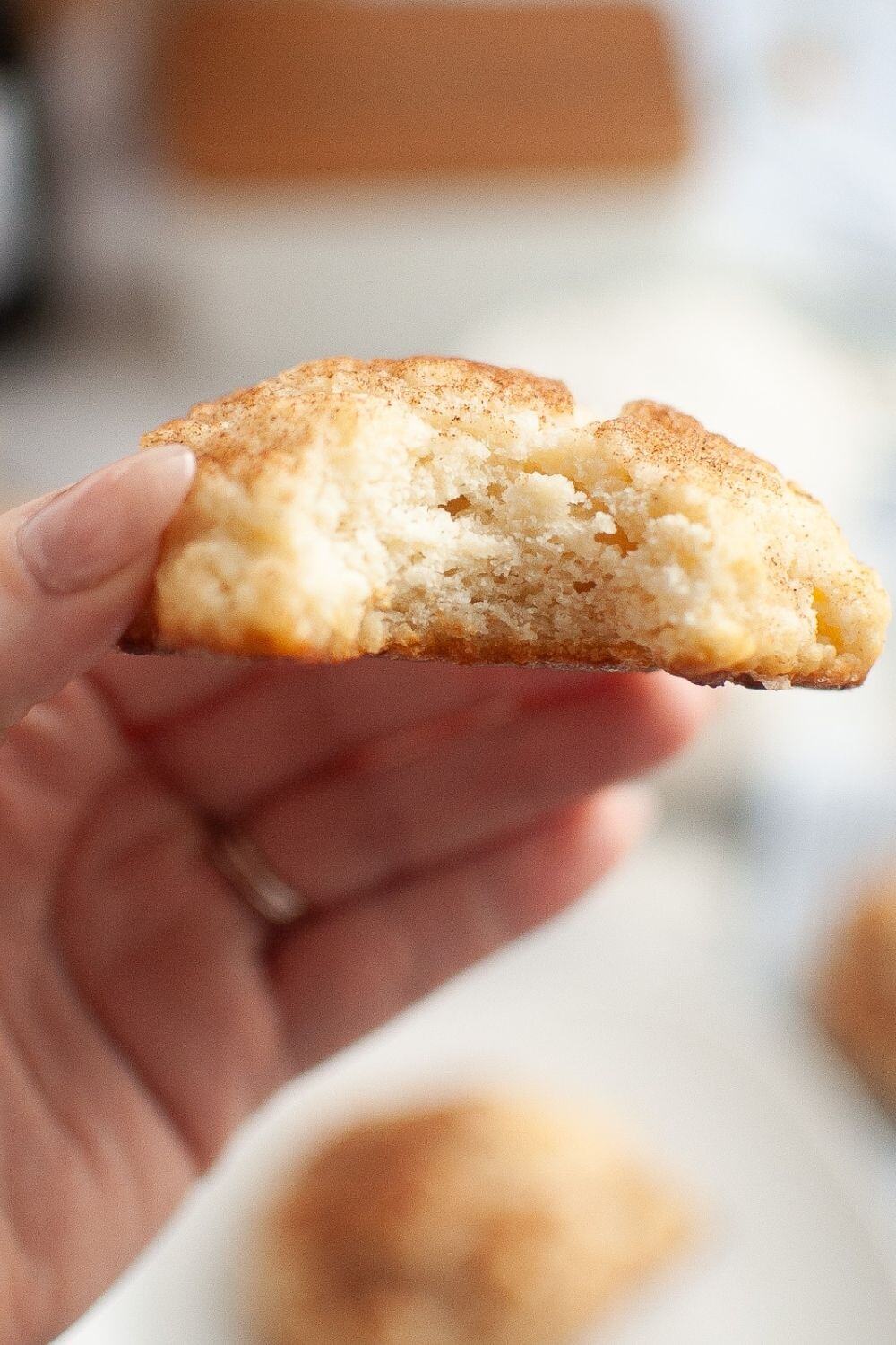 a woman's hand holds a fluffy drop biscuit topped with cinnamon sugar. A bite has been taken out of the biscuit to show the soft, fluffy interior.