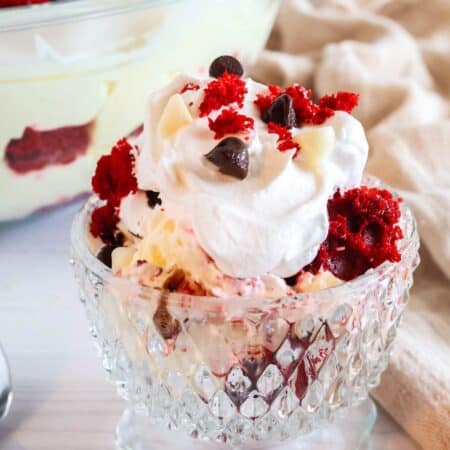 Red velvet trifle served in a glass dessert cup. The trifle is made of red velvet cake, cream cheese pudding cream, whipped cream, and chocolate.
