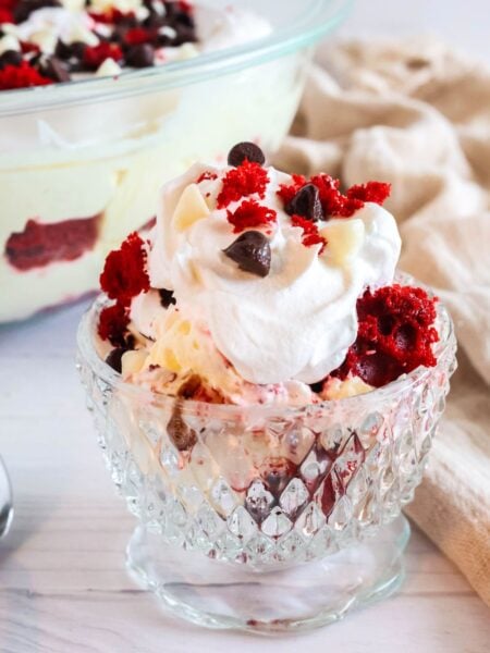 Red velvet trifle served in a glass dessert cup. The trifle is made of red velvet cake, cream cheese pudding cream, whipped cream, and chocolate.