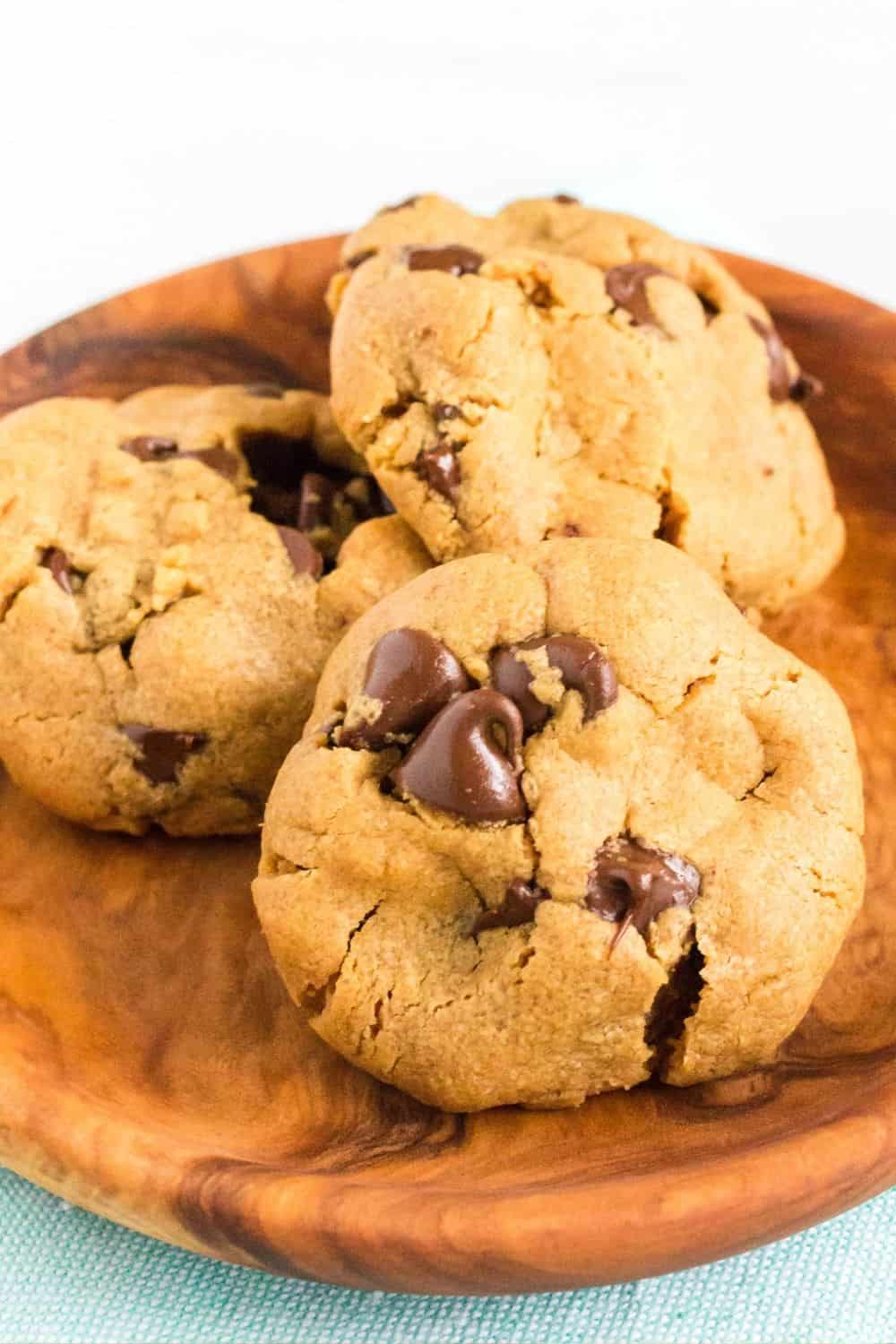 Three simple peanut butter chocolate chip cookies on a small wooden plate.