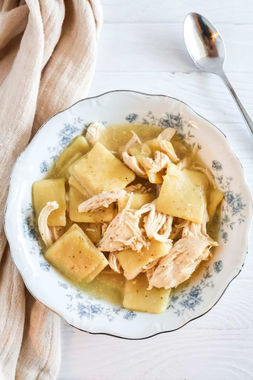 Slow cooker chicken and slicks dumplings served in a patterned china bowl, with a spoon next to the bowl.