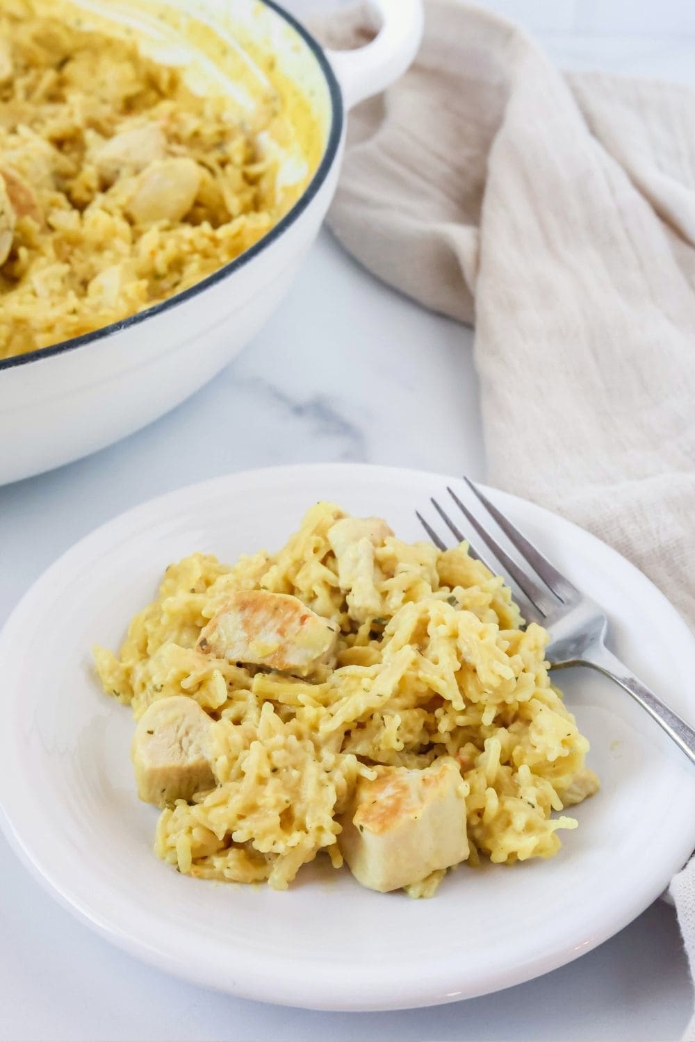 A serving of chicken and Knorr rice on a white plate with a fork. The pan of remaining casserole is in the background.