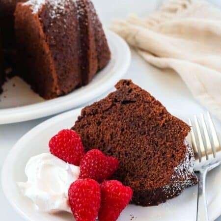 Slice of chocolate pound cake made from cake mix served on a white plate with fresh raspberries and whipped cream.