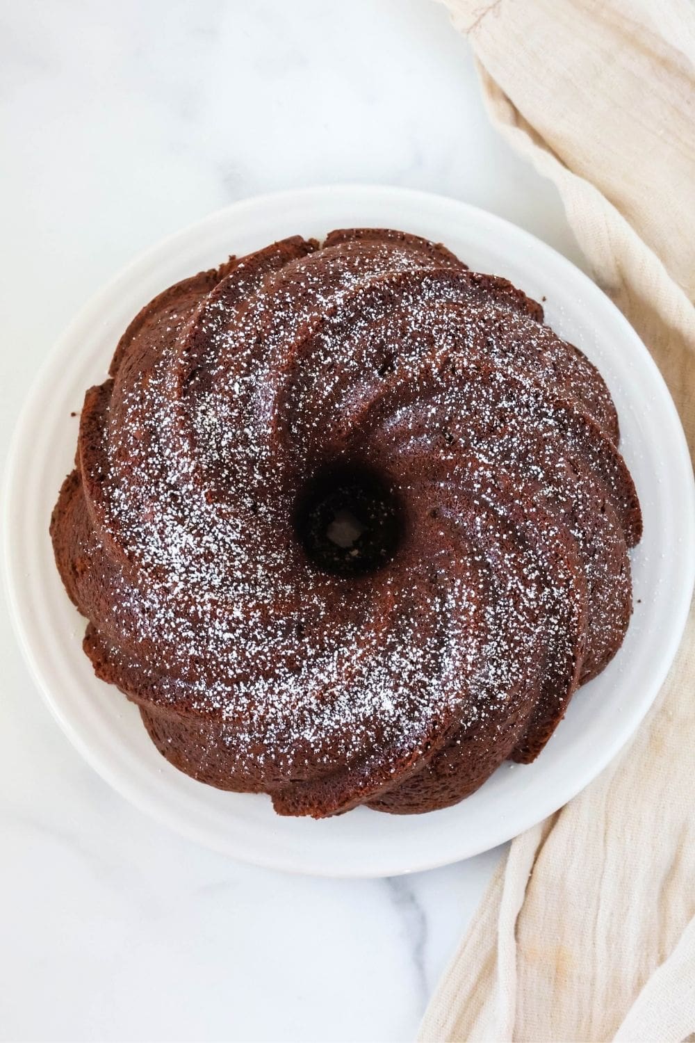 overhead view of a chocolate cream cheese pound cake made without sour cream, served on a white plate and dusted with powdered sugar.