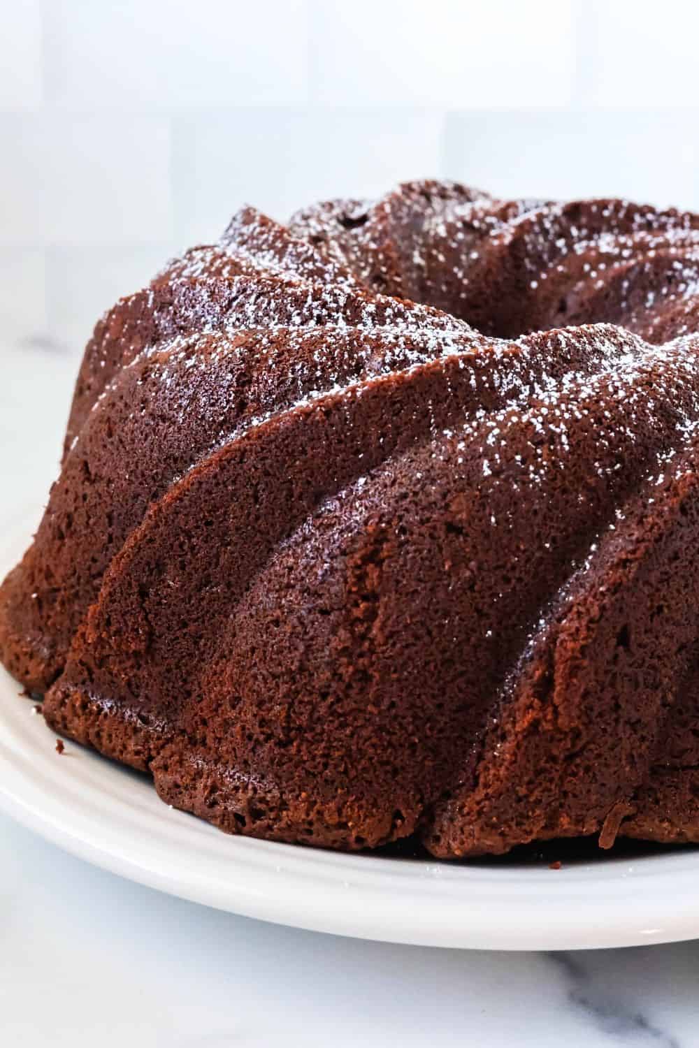 side view of a moist chocolate pound cake dusted with powdered sugar, served on a white plate.