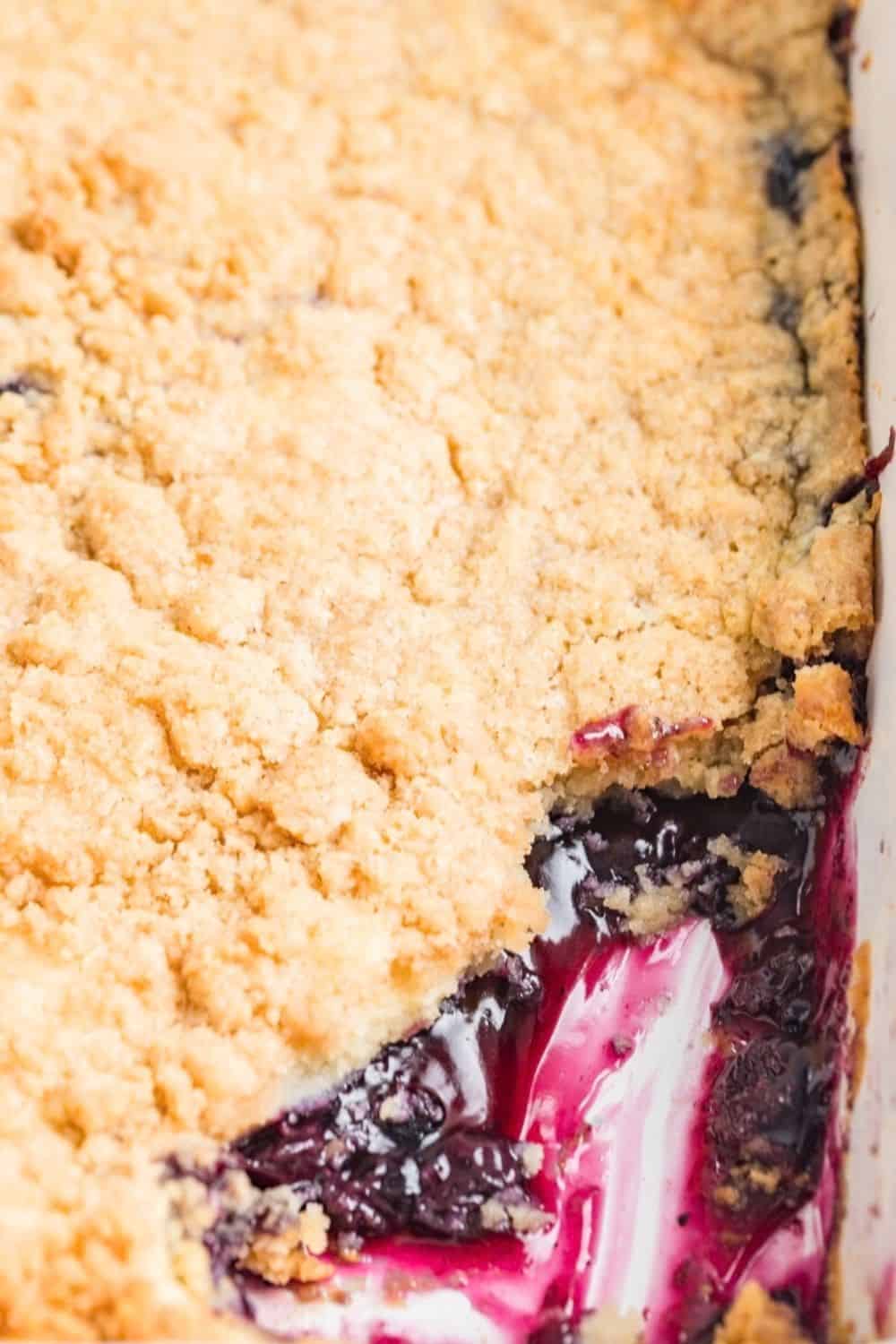 a dish of blueberry dump cake, with some of the dessert scooped out of the dish, showing the warm filling under the golden crust.