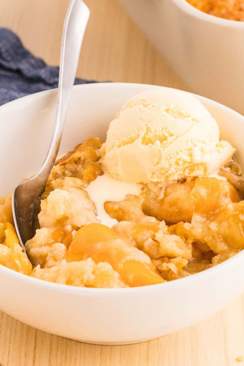 cake mix peach cobbler dump cake in a white bowl, topped with a scoop of vanilla ice cream. A spoon is in the bowl.
