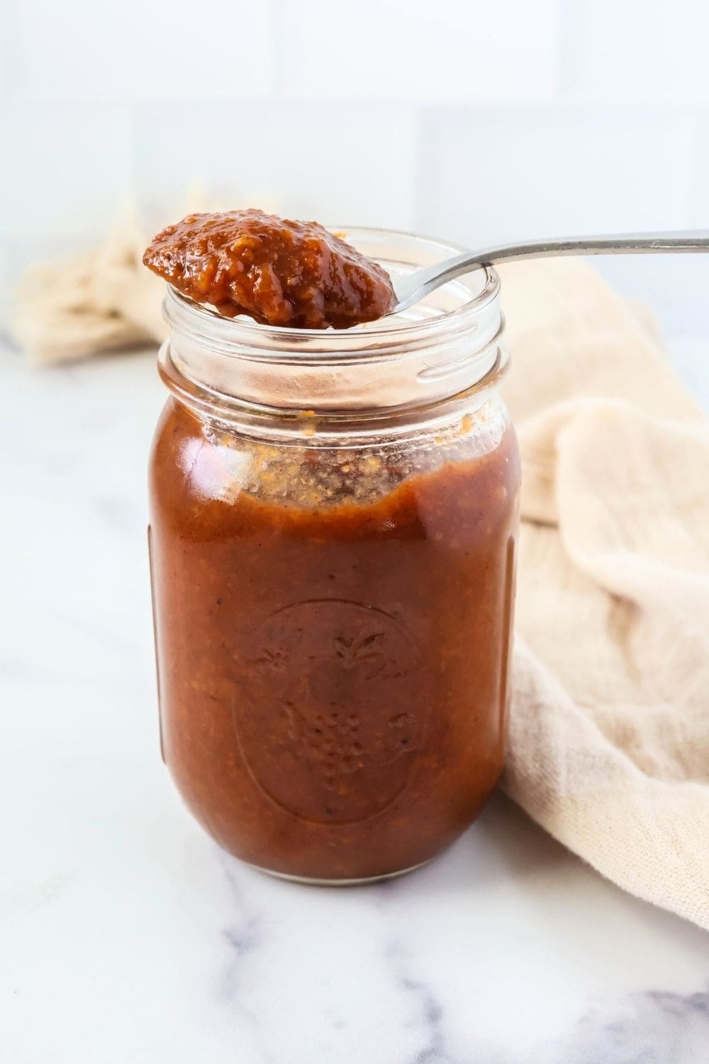 a jar of Crock Pot peach butter, with a spoon of homemade peach butter resting on the rim of the jar.